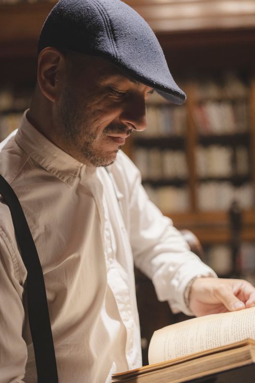 Free A man in a stylish hat reading a book in a warm, inviting library. Stock Photo