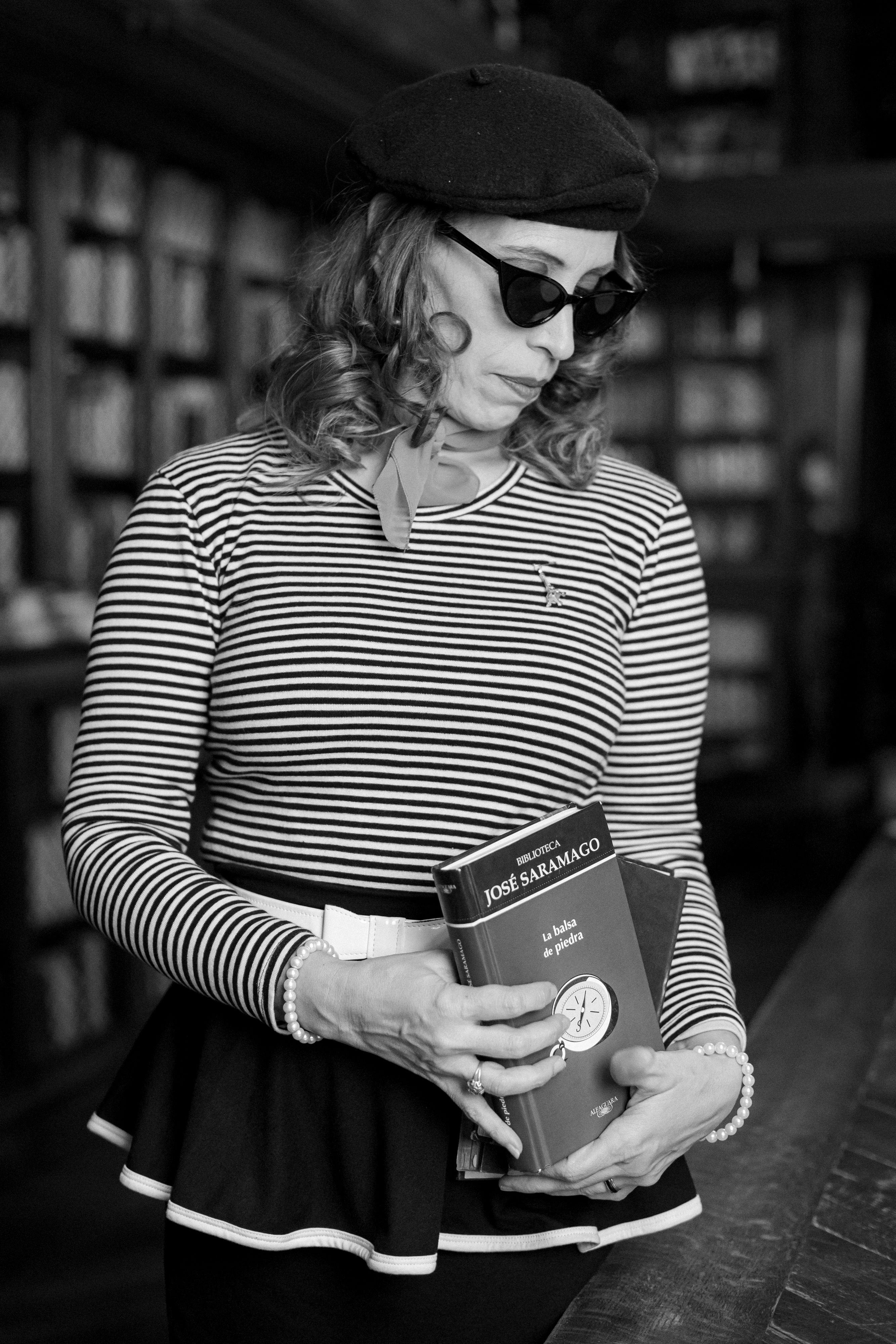 Elegant woman with vintage style holding José Saramago book in a classic library.