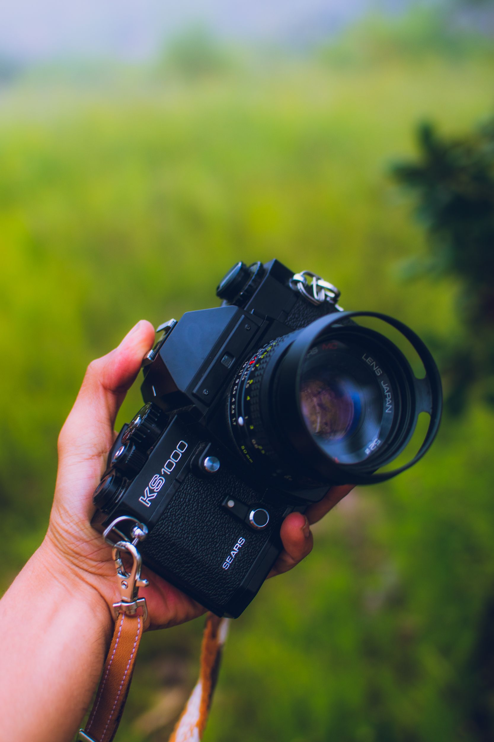 Close-up of a vintage film camera being held outdoors with a green background.