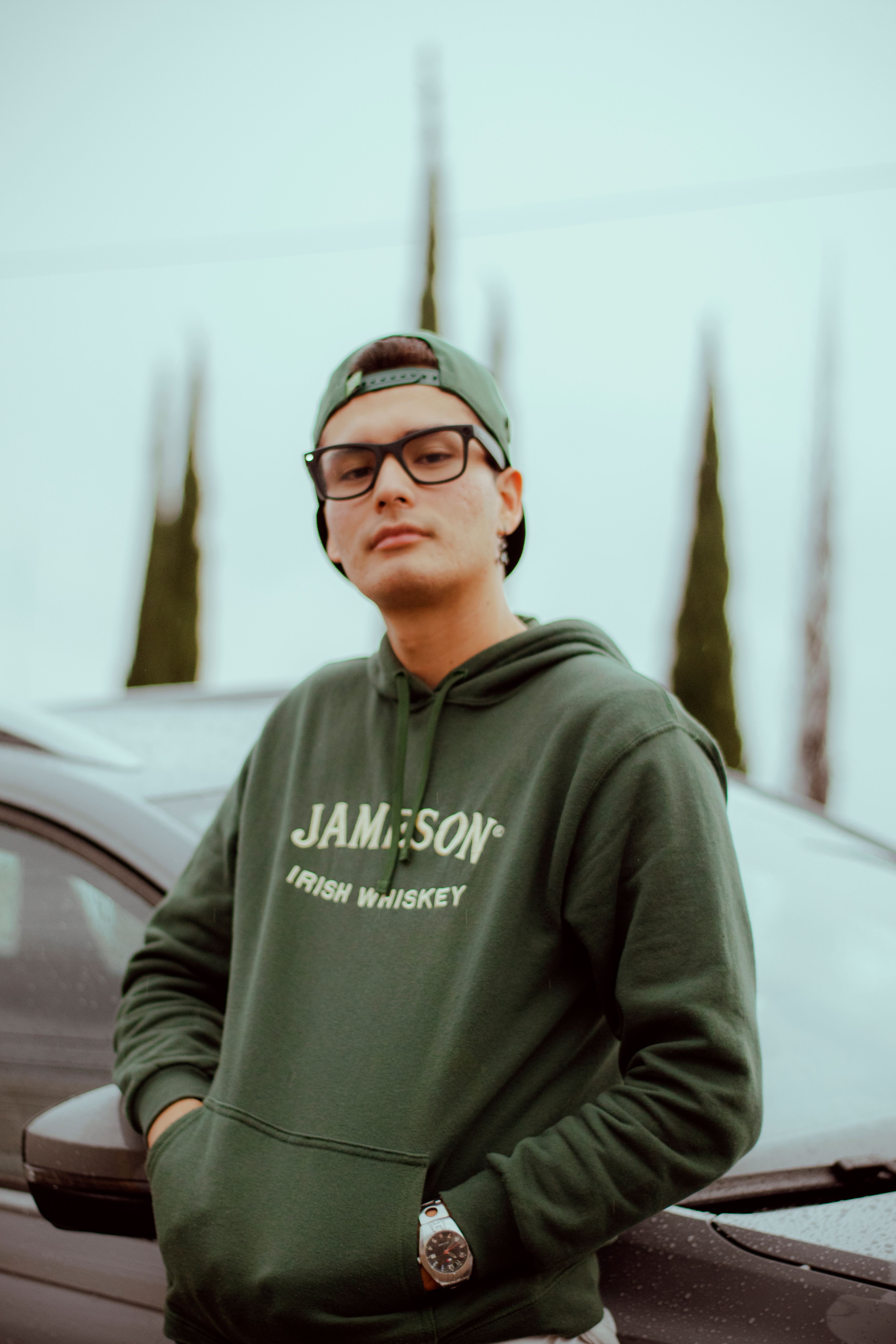 Confident young adult wearing a green hoodie outdoors with a casual pose near a car.