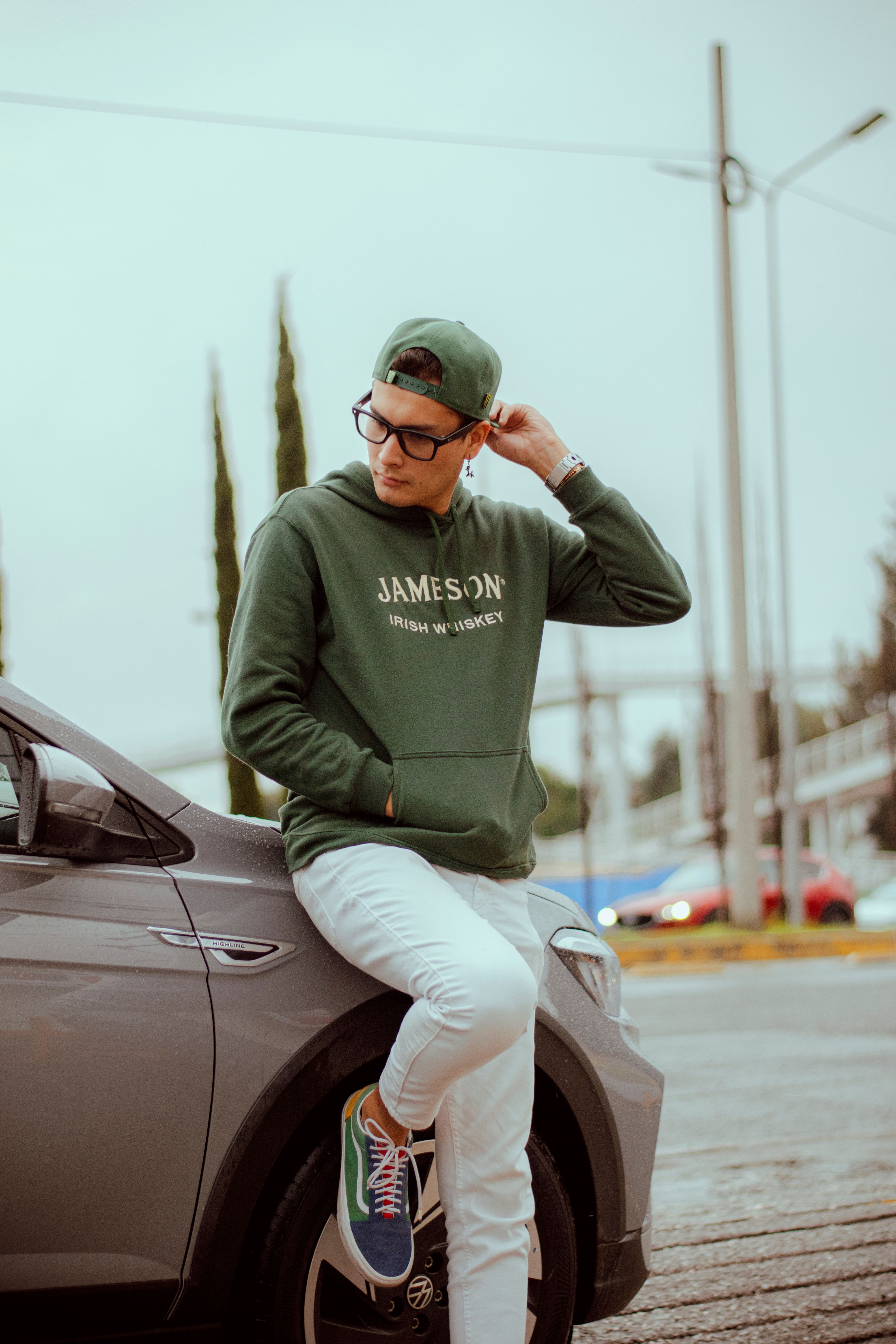Stylish young man in casual wear leans on a car outdoors, exuding relaxed confidence.