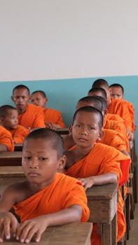 A group of young monks in orange robes attentively sitting in a classroom in Cambodia.