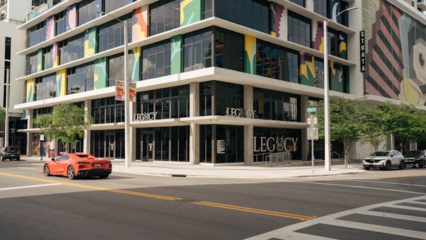 Modern building with vibrant facade on a sunny day, featuring a red sports car and street view.