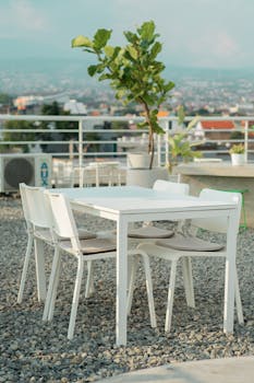 Modern white table and chairs on a rooftop overlooking cityscape in daylight.