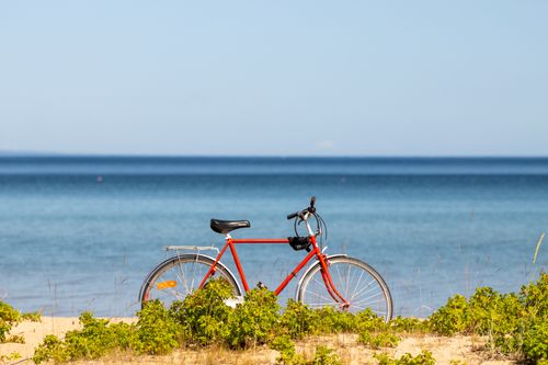 Free A vibrant red bicycle parked on a sunny beach with clear blue water in Jönköping, Sweden. Stock Photo