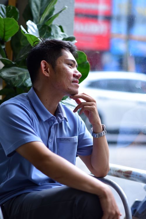 Free A man in a blue shirt sits by a cafe window, lost in thought. Stock Photo