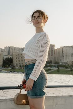 A woman stands on a rooftop with an urban skyline in the background, enjoying the evening breeze.