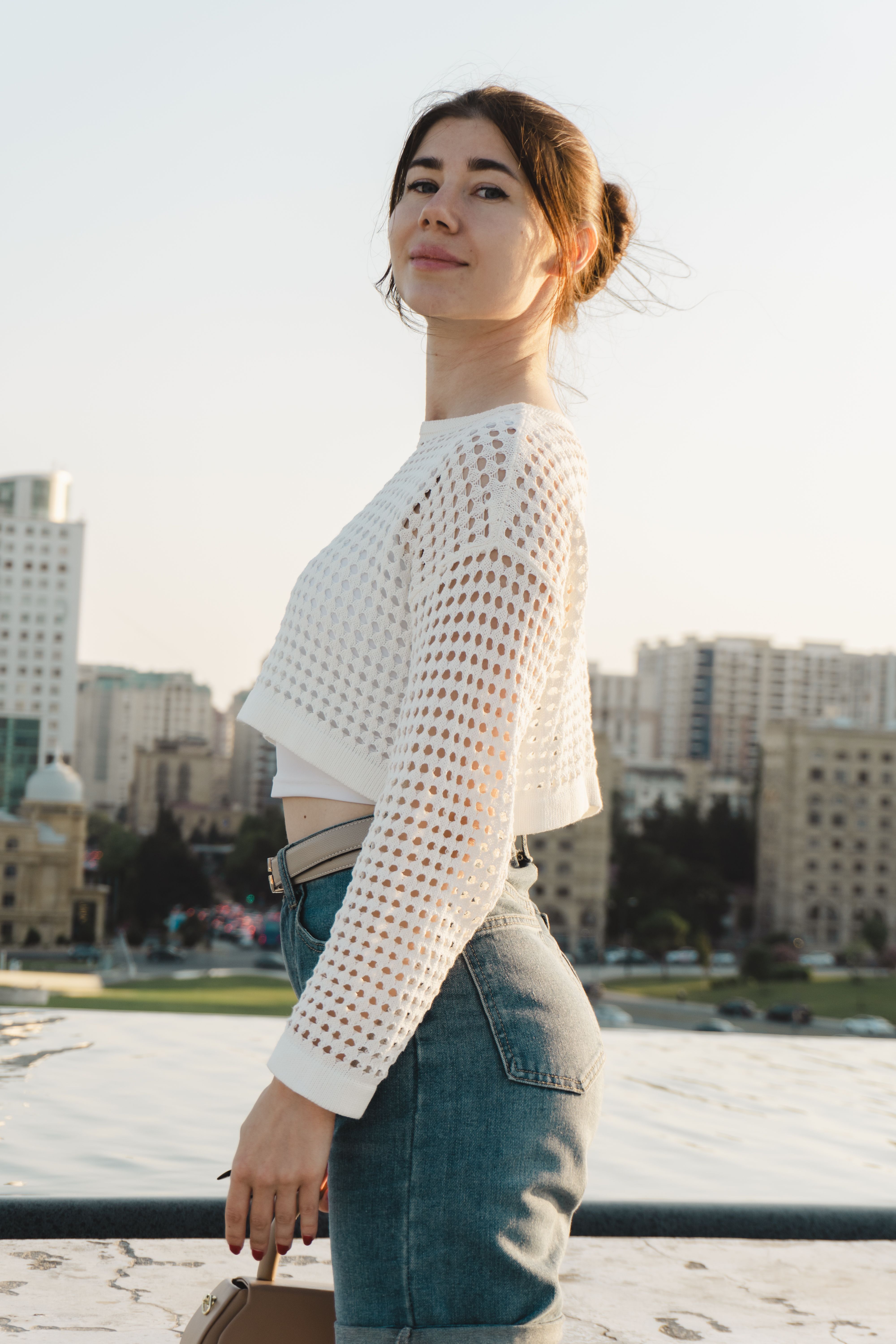 Woman in stylish attire posing in a modern cityscape with buildings in the background during daytime.