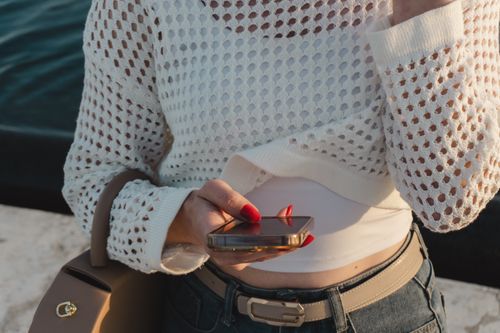 Free Close-up of a woman checking her smartphone in casual, stylish attire with bright sunlight. Stock Photo