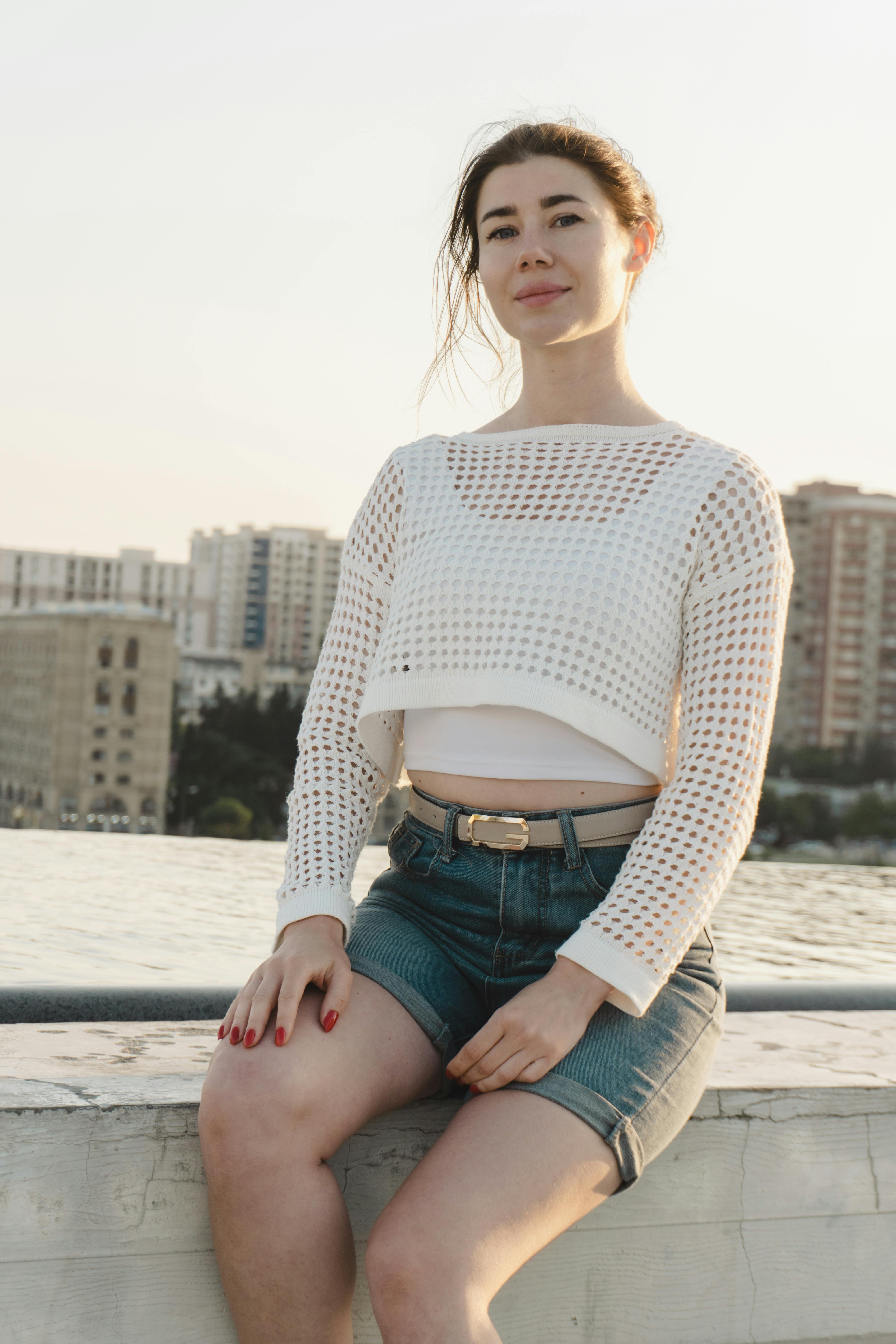 Young woman in casual attire posing outdoors against a cityscape at sunset.