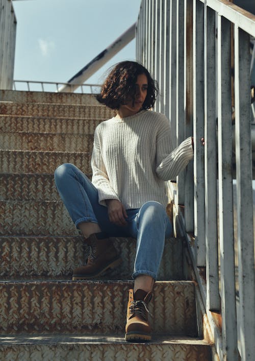 Woman Wearing White Sweater and Blue Jeans Sitting on Stairs