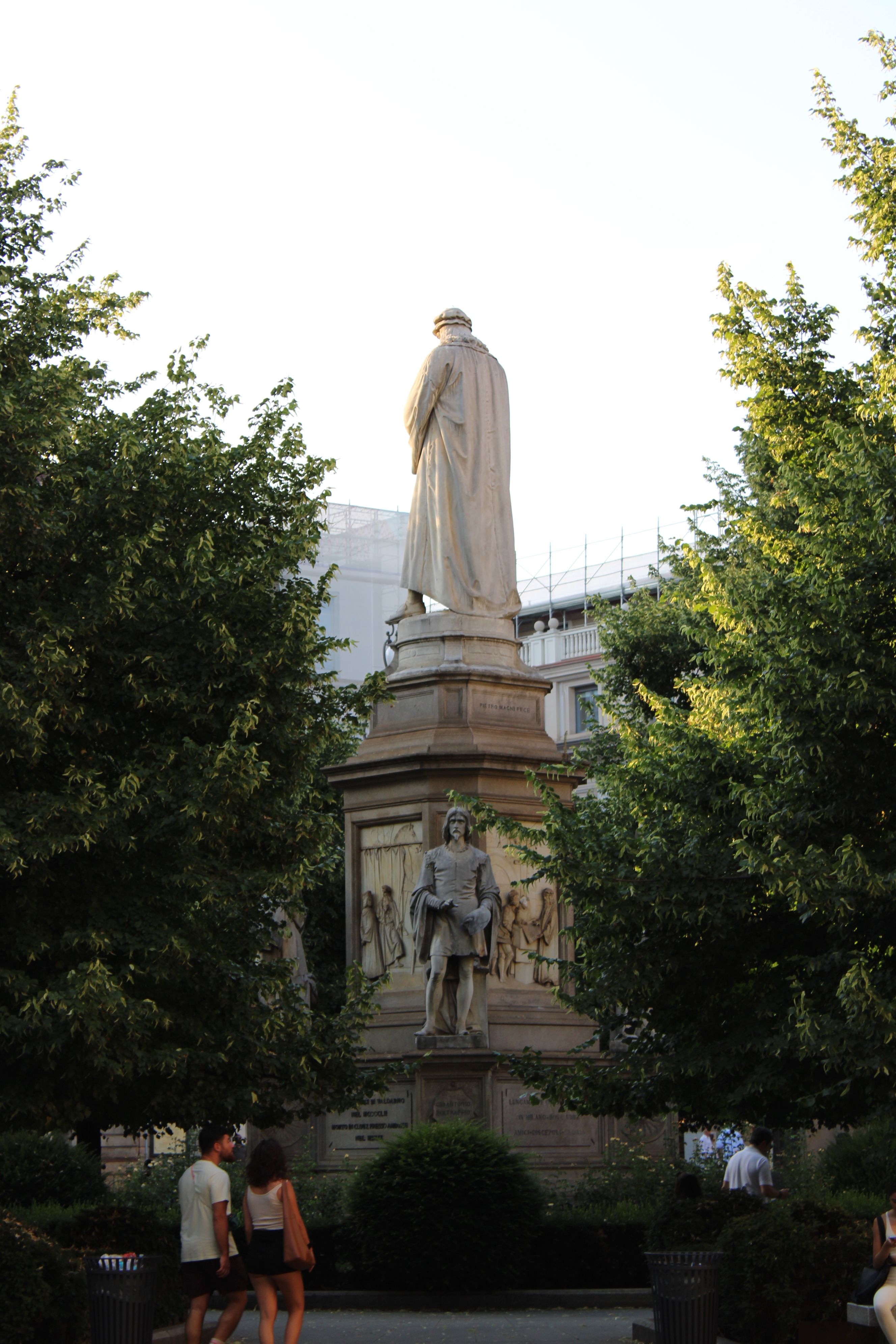 A grand statue surrounded by lush greenery at Piazza del Duomo, Milan, Italy, captured during the day.
