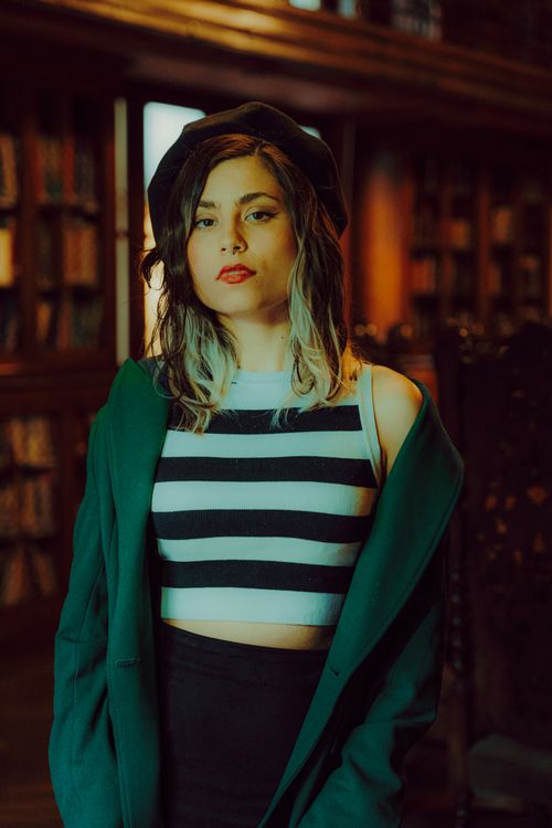 Free A stylish woman poses confidently in a library wearing a striped top and beret. Stock Photo