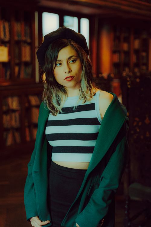 Free Elegant woman in a beret and striped top at a library, reflecting French-inspired style. Stock Photo