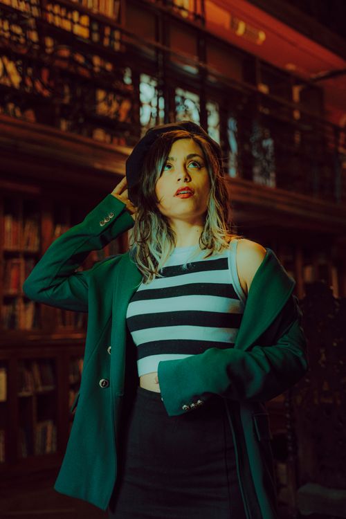 Free A fashionable woman poses confidently in a library, sporting a green blazer and striped top. Stock Photo