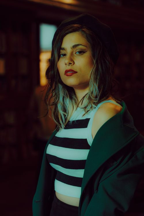 Free A fashionable person with long hair poses confidently indoors, wearing a striped crop top and jacket. Stock Photo