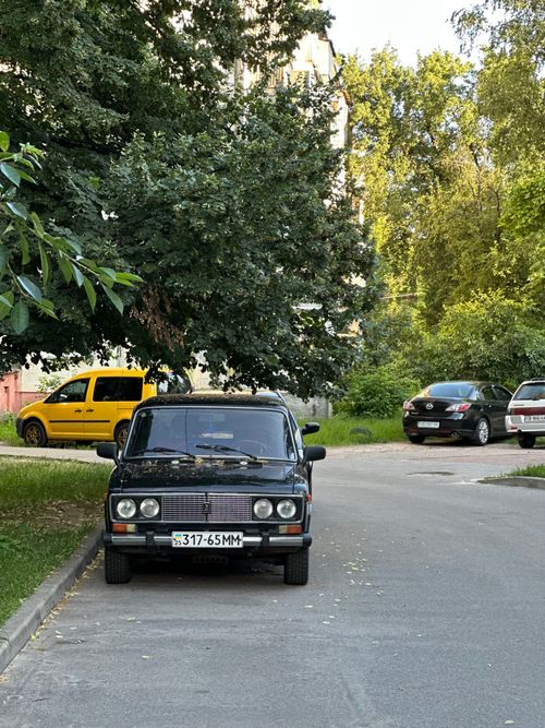 Free Retro car parked on a tranquil street with trees and modern cars nearby. Stock Photo