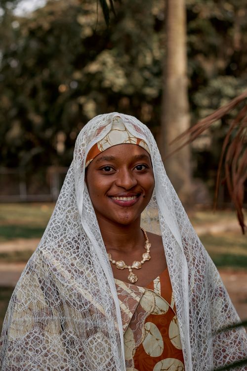 Free Woman with lace veil and necklace smiling outdoors. Bright attire. Stock Photo