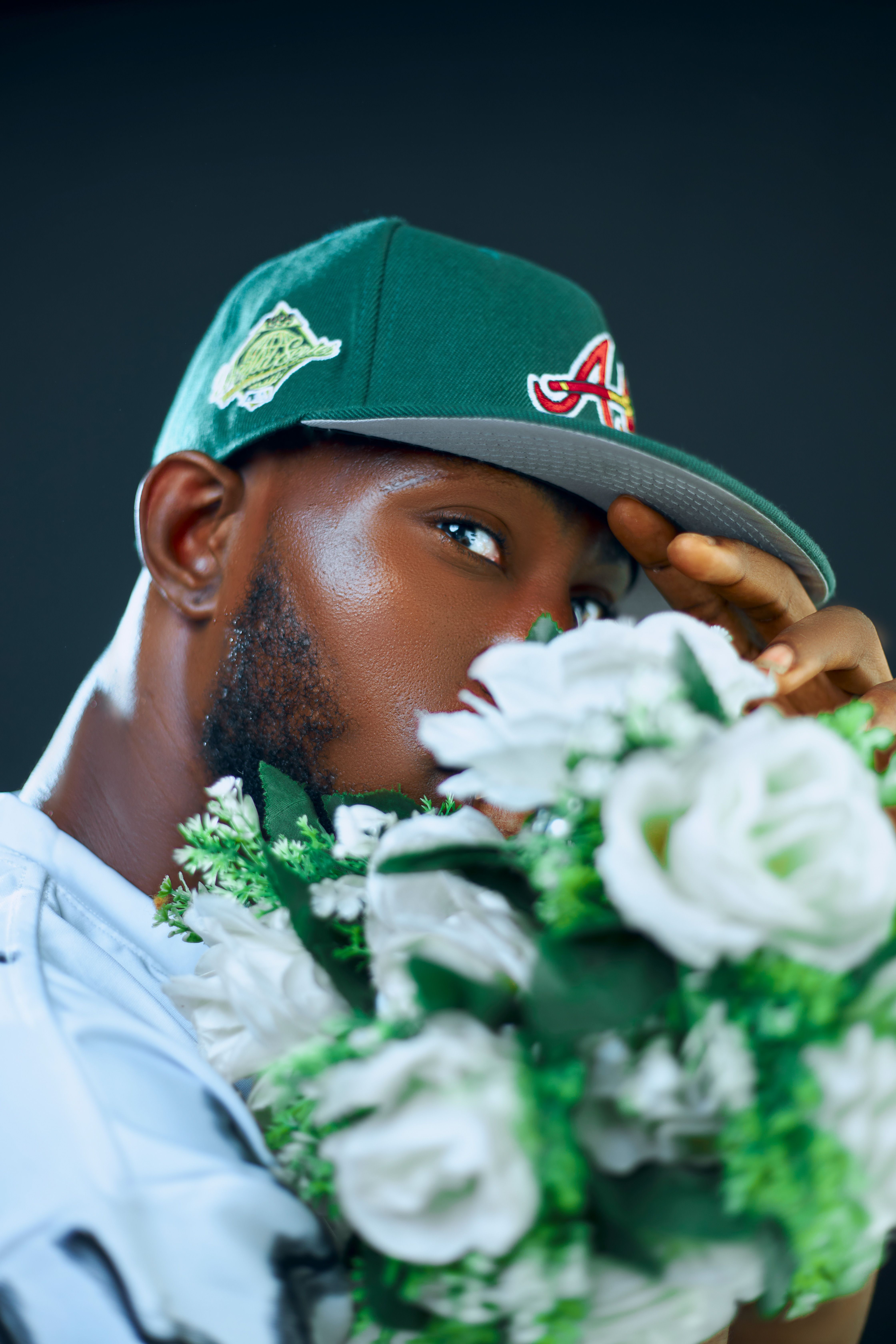 A stylish man in a green cap holding white flowers in an artistic portrait.