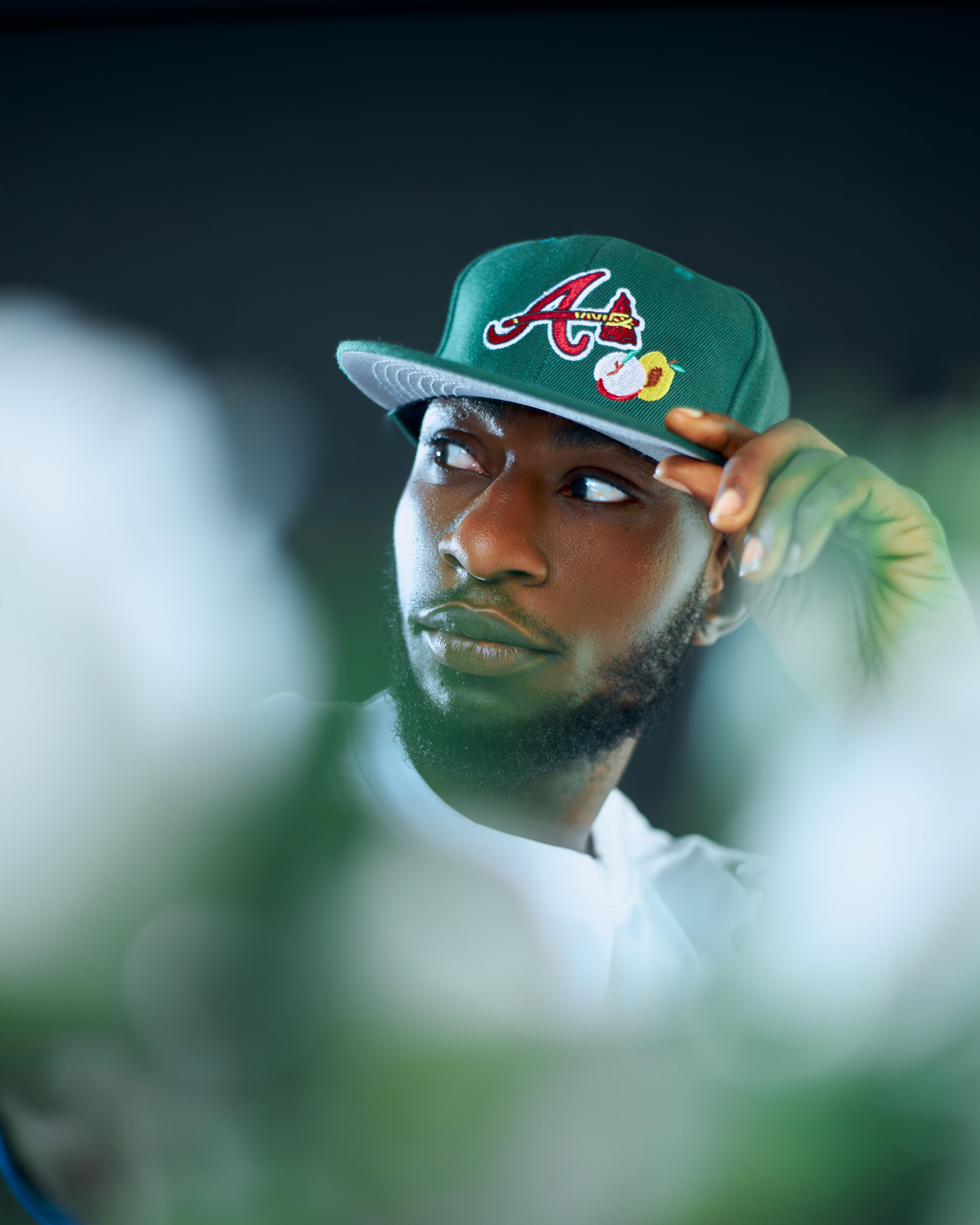 Close-up portrait of a man wearing a green cap, with a soft focus foreground, and a thoughtful expression.