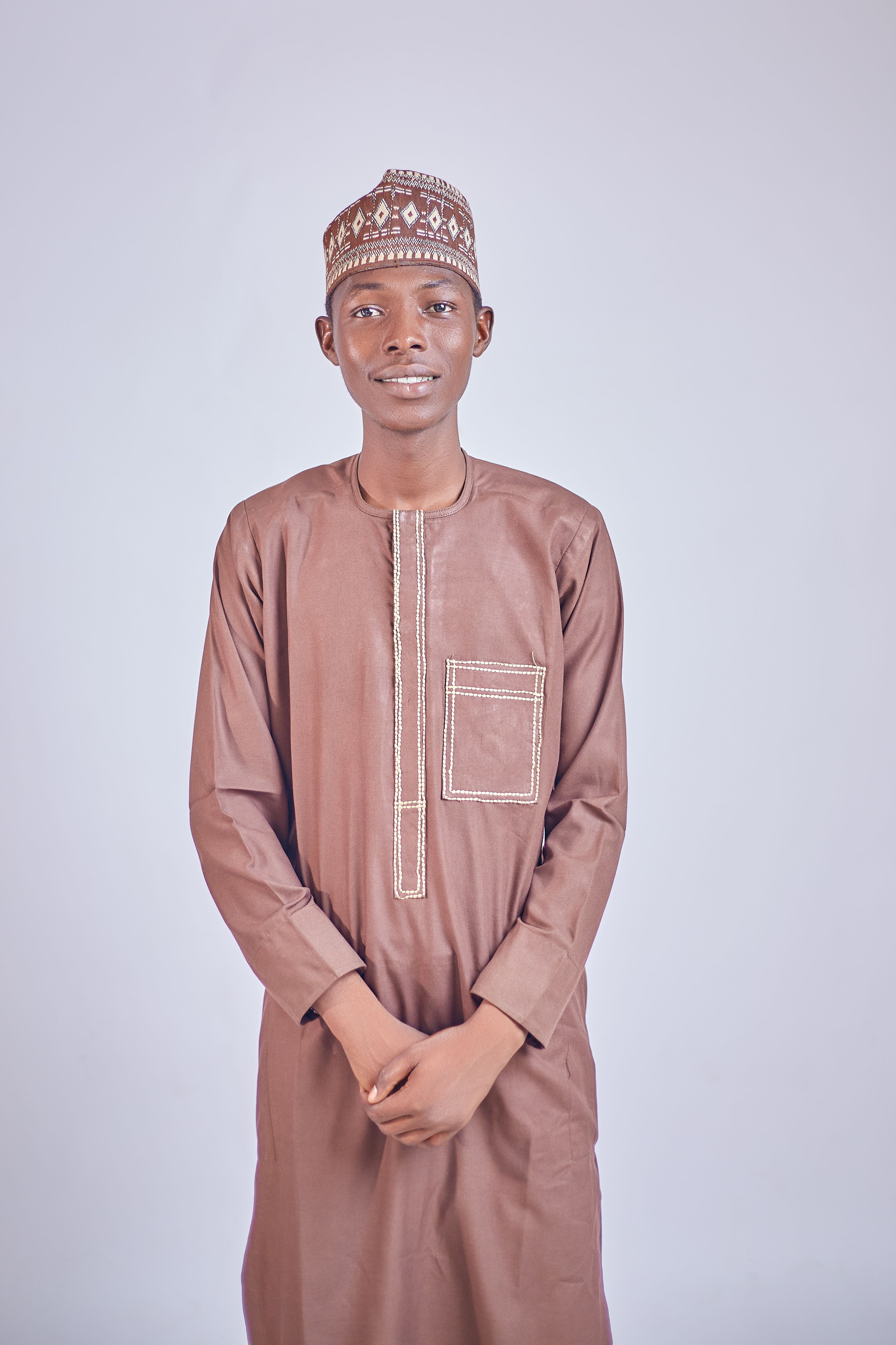Portrait of a young man in traditional African clothing standing against a plain background.