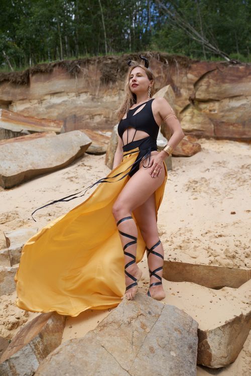 Free Elegant woman in swimsuit poses on a rocky sandstone beach wearing a flowing yellow skirt. Stock Photo
