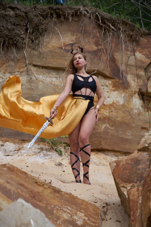Free A woman in warrior costume with a sword poses regally in a rocky desert setting. Stock Photo