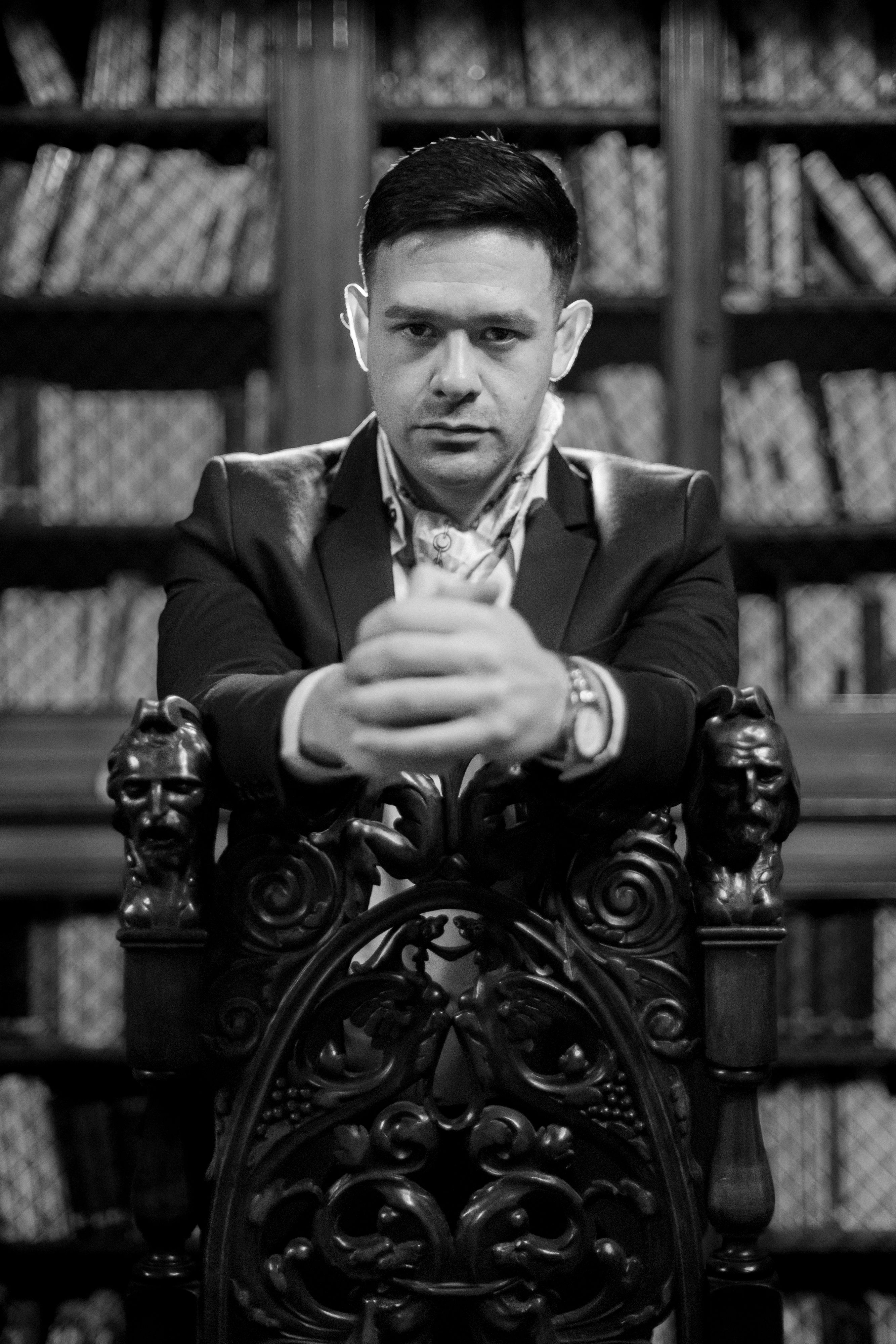 A sophisticated black and white portrait of a man in a classic library setting, exuding style and confidence.