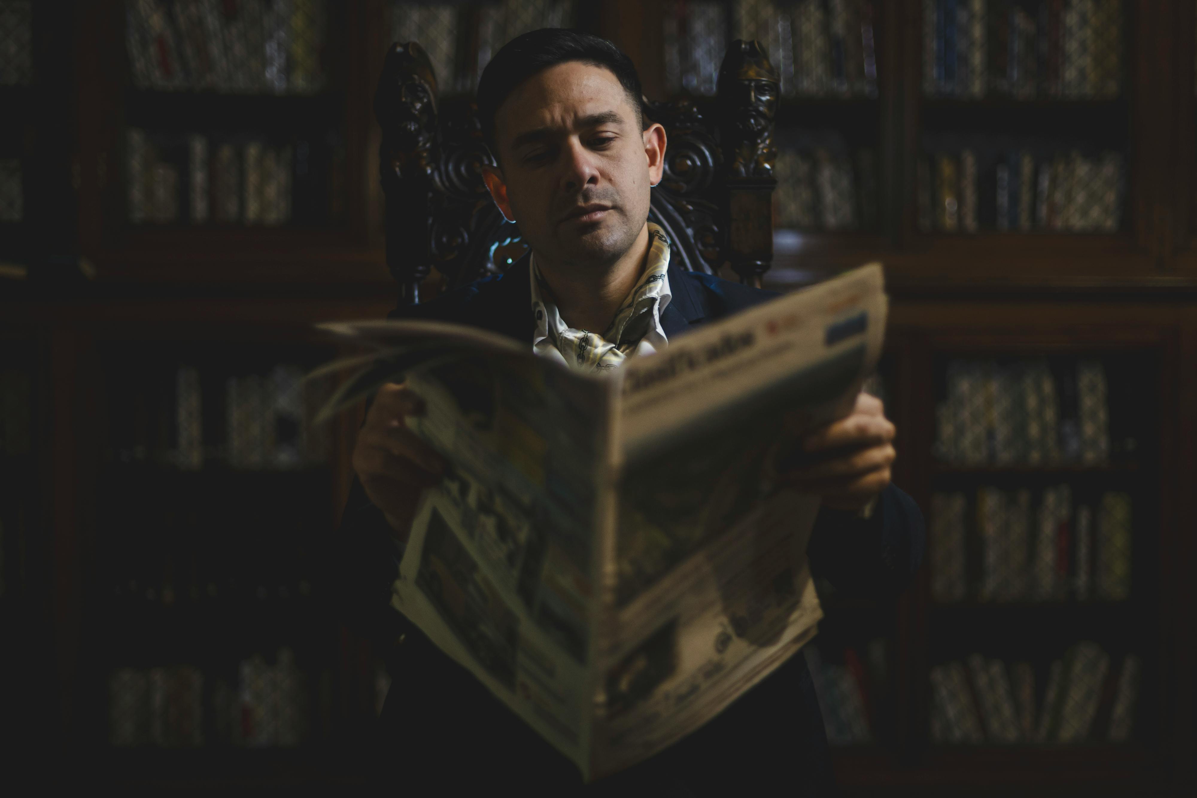 A man reads a newspaper in an elegant library setting, exuding sophistication and knowledge.