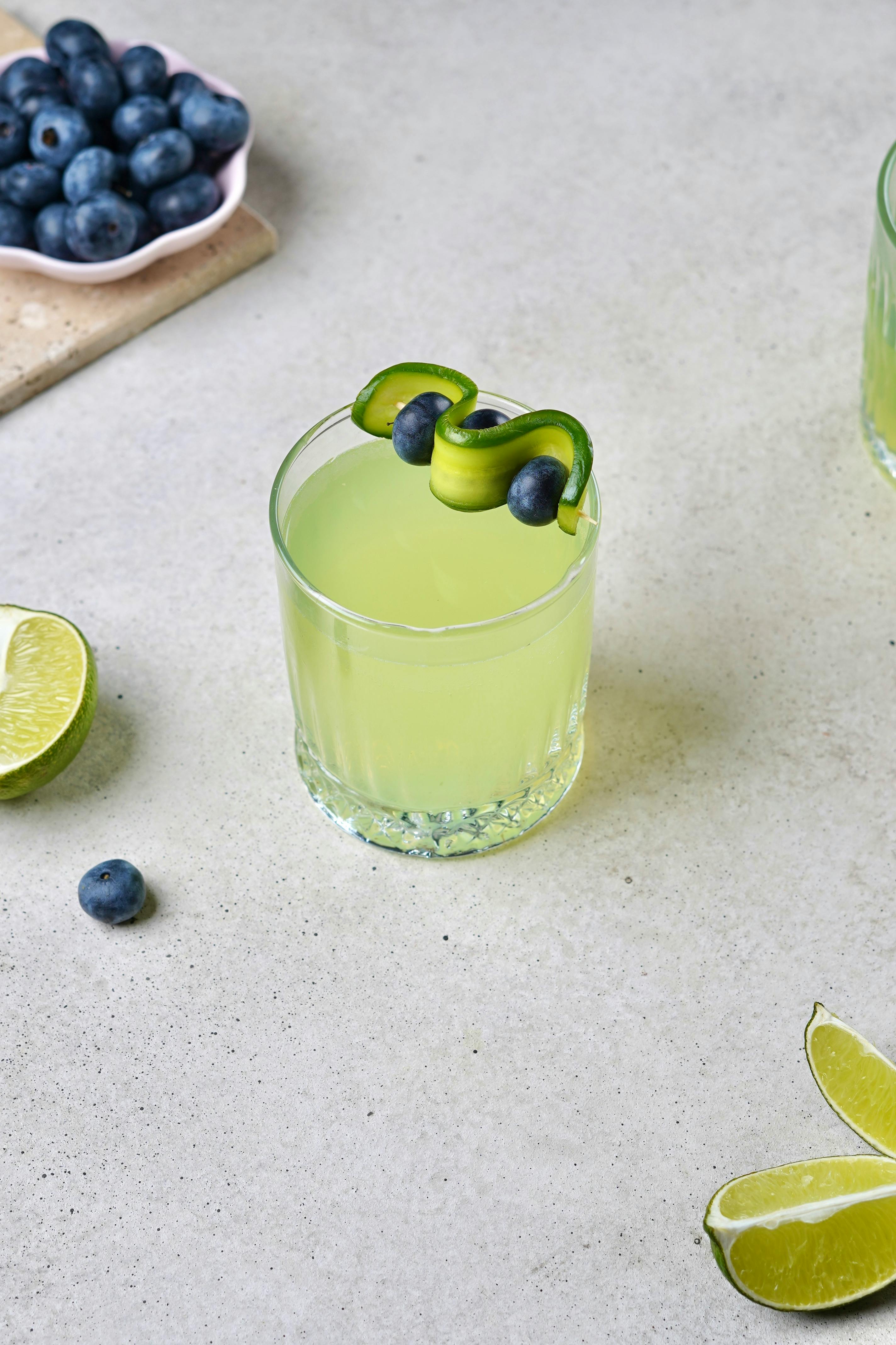 Lime cocktail with blueberry and cucumber garnish on a light background, perfect for summer.