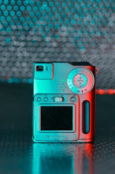 Close-up of a vintage digital camera highlighted by vibrant red and blue neon lights.