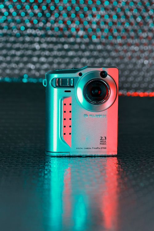 Free A vintage digital camera illuminated by vibrant teal and red neon lights, creating a unique retro style. Stock Photo