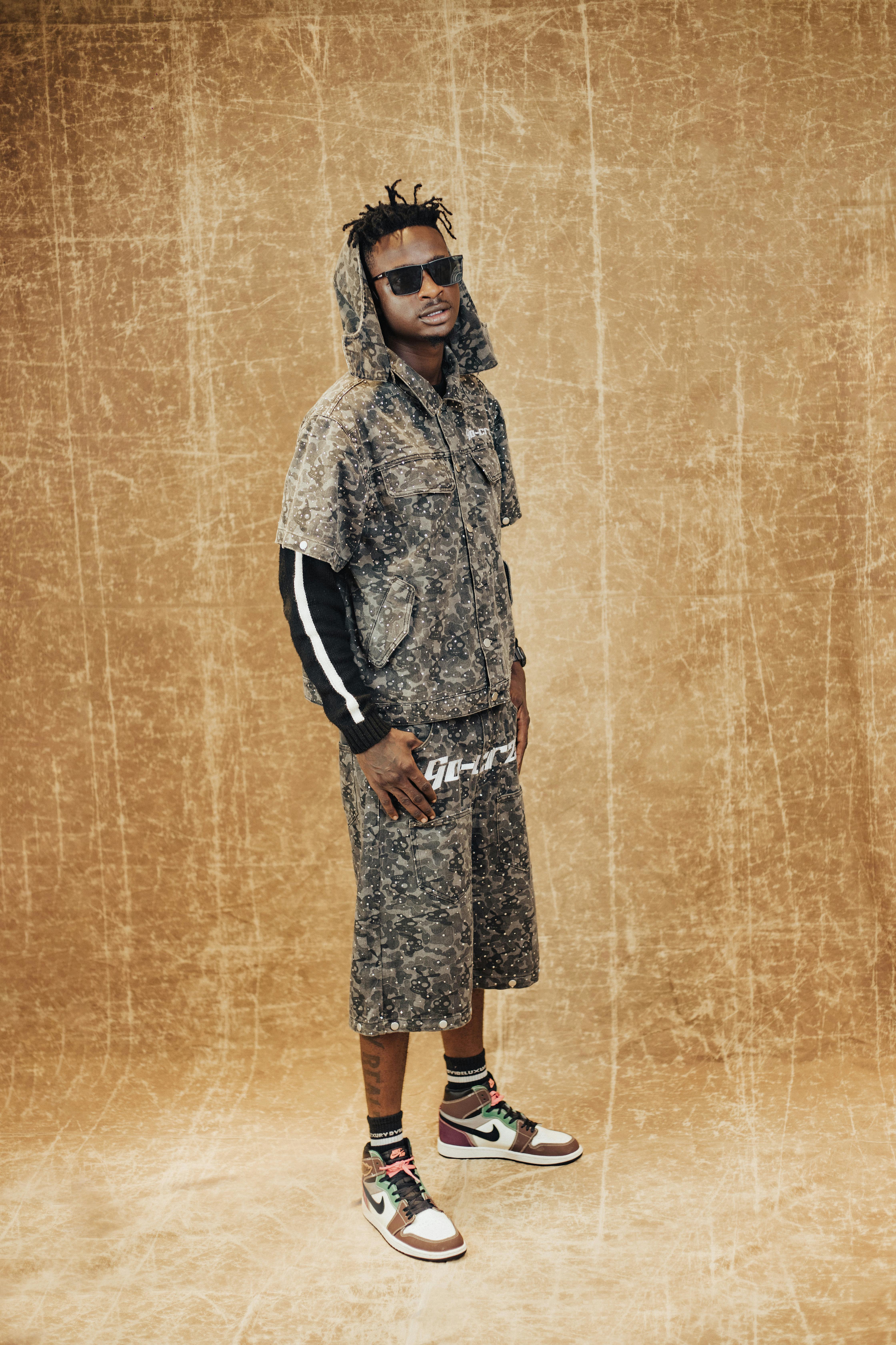 Stylish man wearing a trendy camo outfit and sunglasses standing confidently indoors.