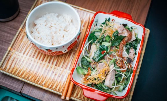 Delicious Asian dish featuring rice with a flavorful pork and vegetable salad served on a bamboo tray.