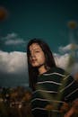 一位年轻女子留着长发，在户外以多云天空为背景摆姿势