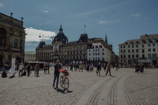 Scenic view of a bustling city square in Copenhagen with historical buildings and people enjoying a sunny day.