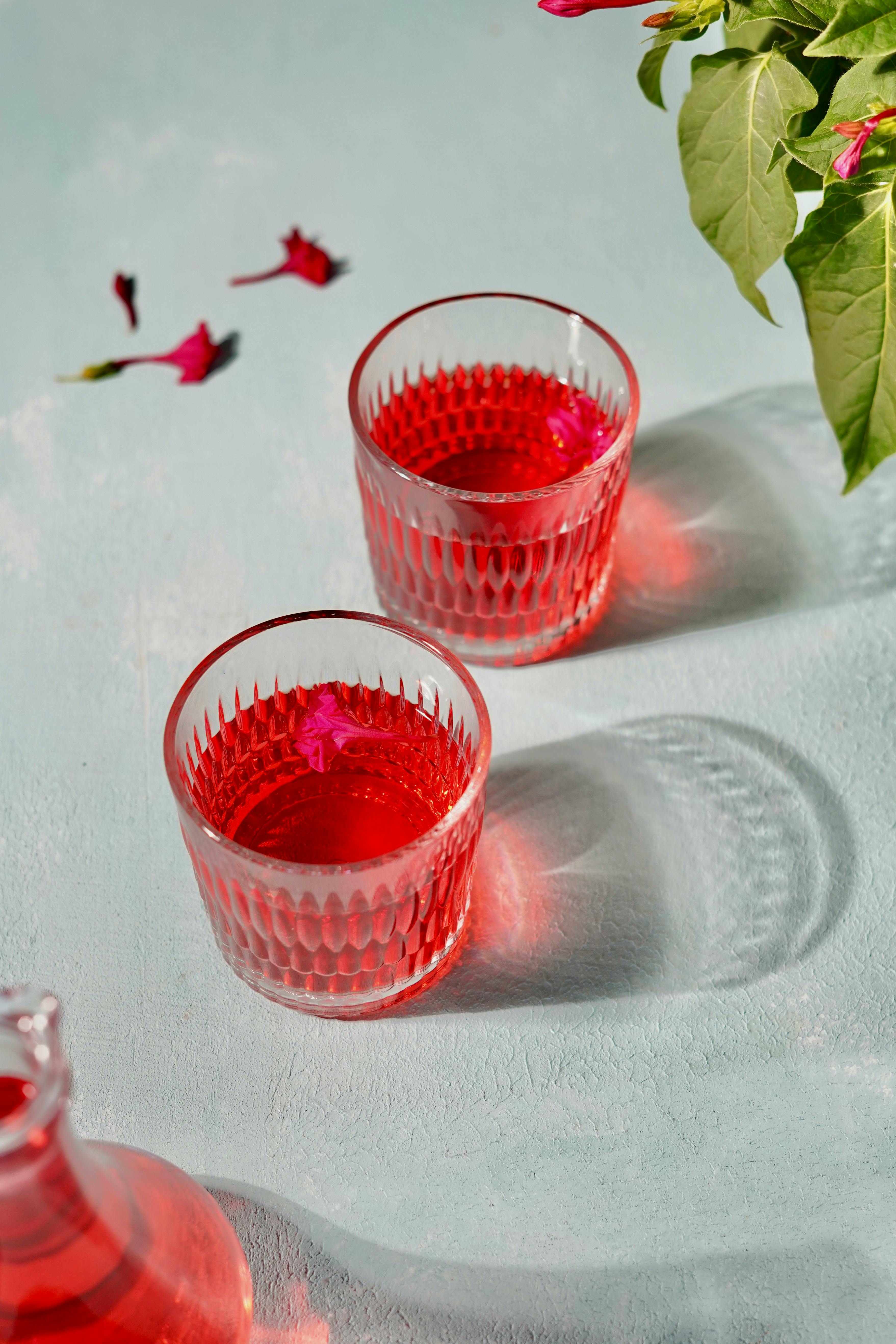 Two elegant glasses of vibrant hibiscus tea with petals, offering a refreshing visual appeal.