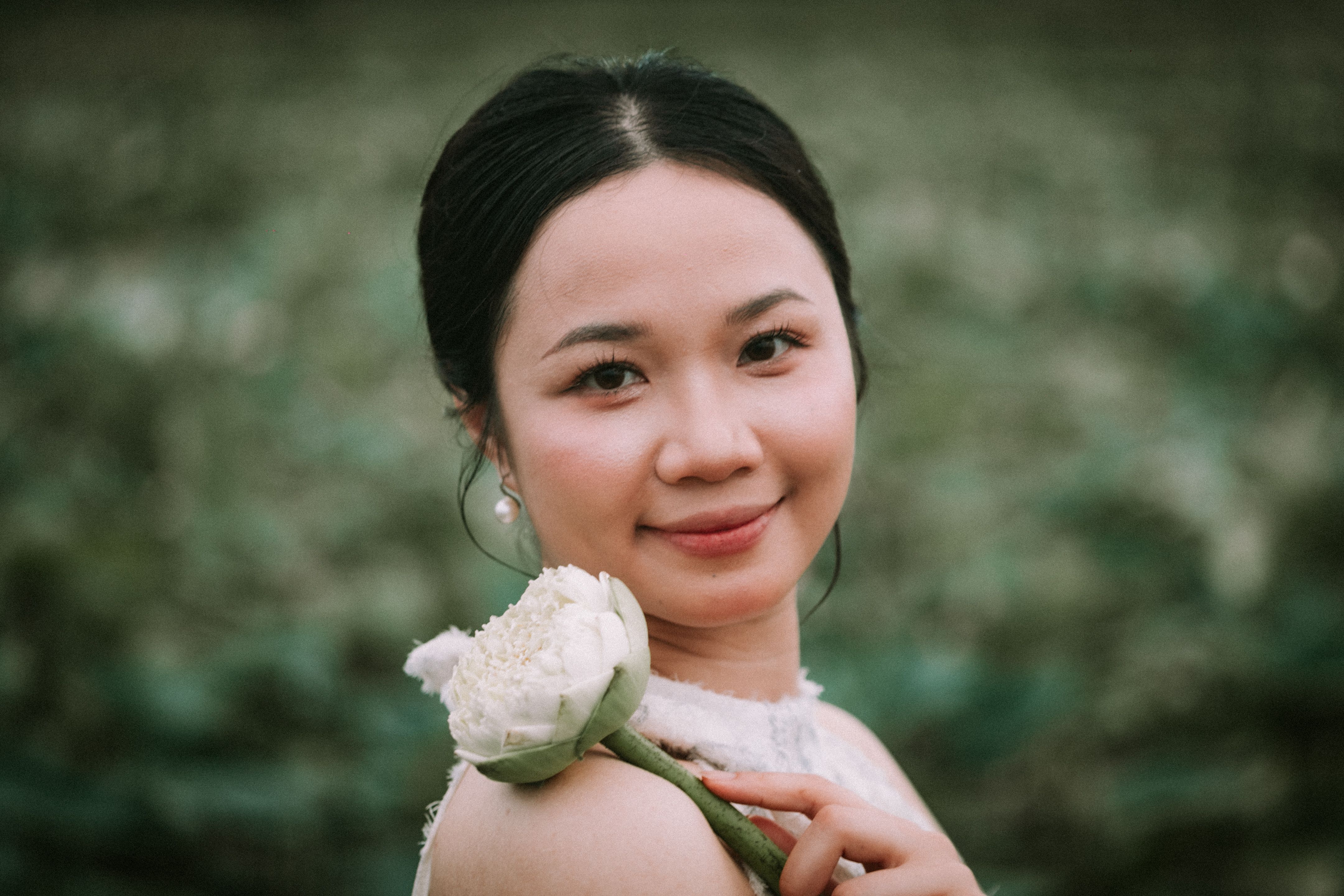 A serene portrait of a woman holding a white lotus outdoors in Hải Phòng, Vietnam.