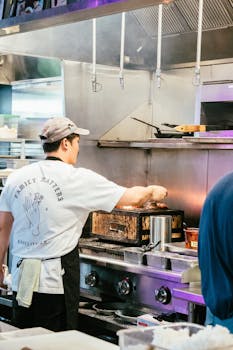 A chef in a bustling kitchen preparing food, showcasing culinary skills and fine dining atmosphere.