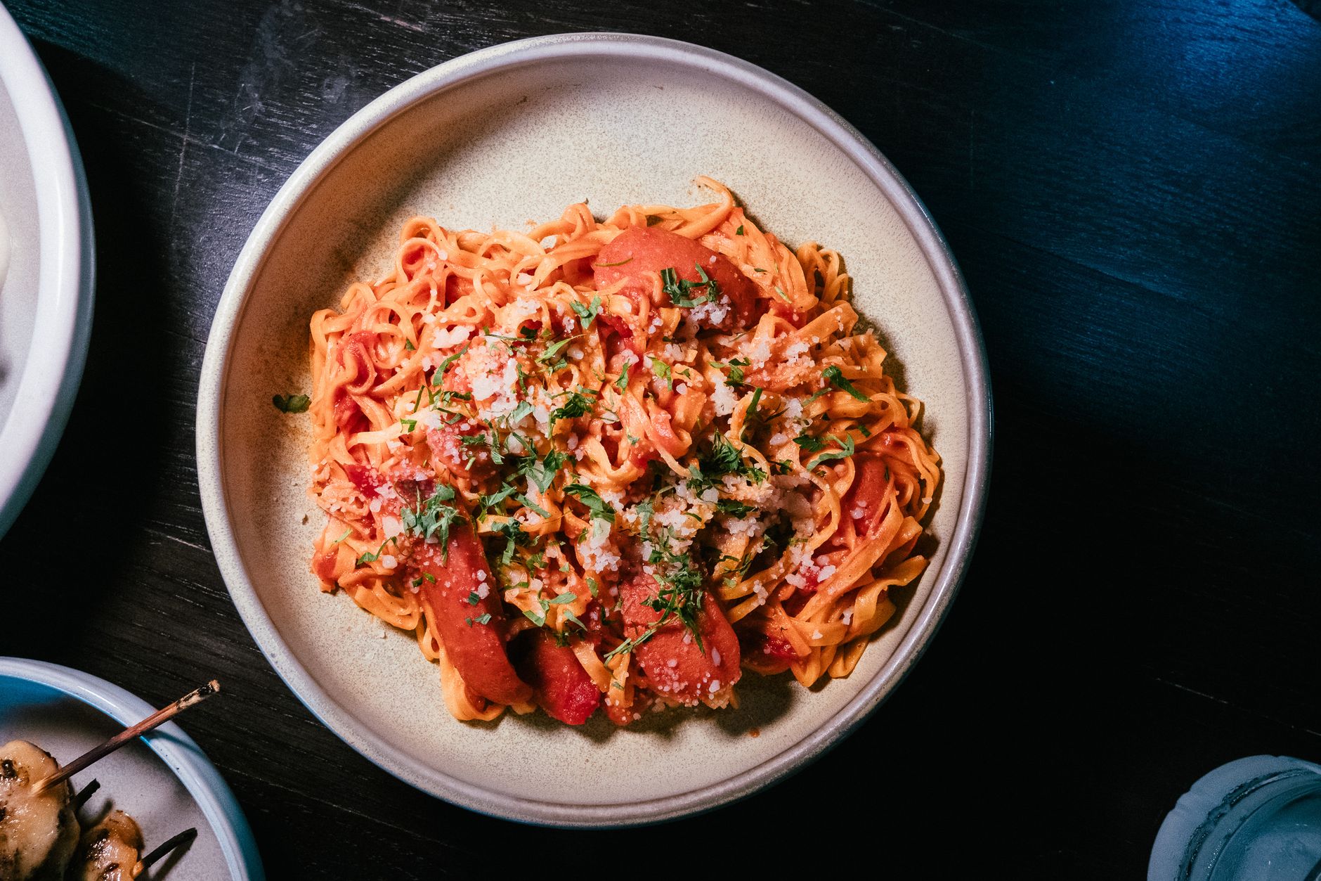 A steaming bowl of fresh Turkish noodles glossed with deep red pepper sauce, topped with crumbled white beyaz peynir, golden crispy garlic pieces, and bright green fresh parsley