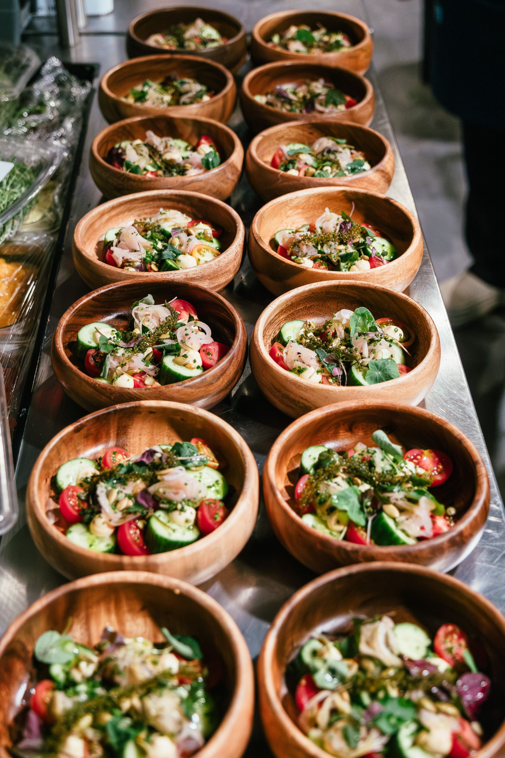 Fresh salads in wooden bowls, featuring cucumbers, cherry tomatoes, and greens, perfect for catering events.