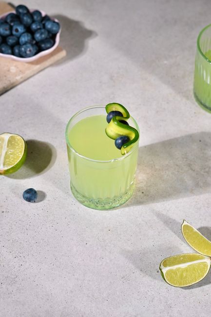 Lime juice with cucumber and blueberry garnish on a concrete surface, ideal for summer refreshment.