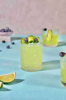 Vibrant cucumber lime cocktail garnished with blueberries on textured surface.