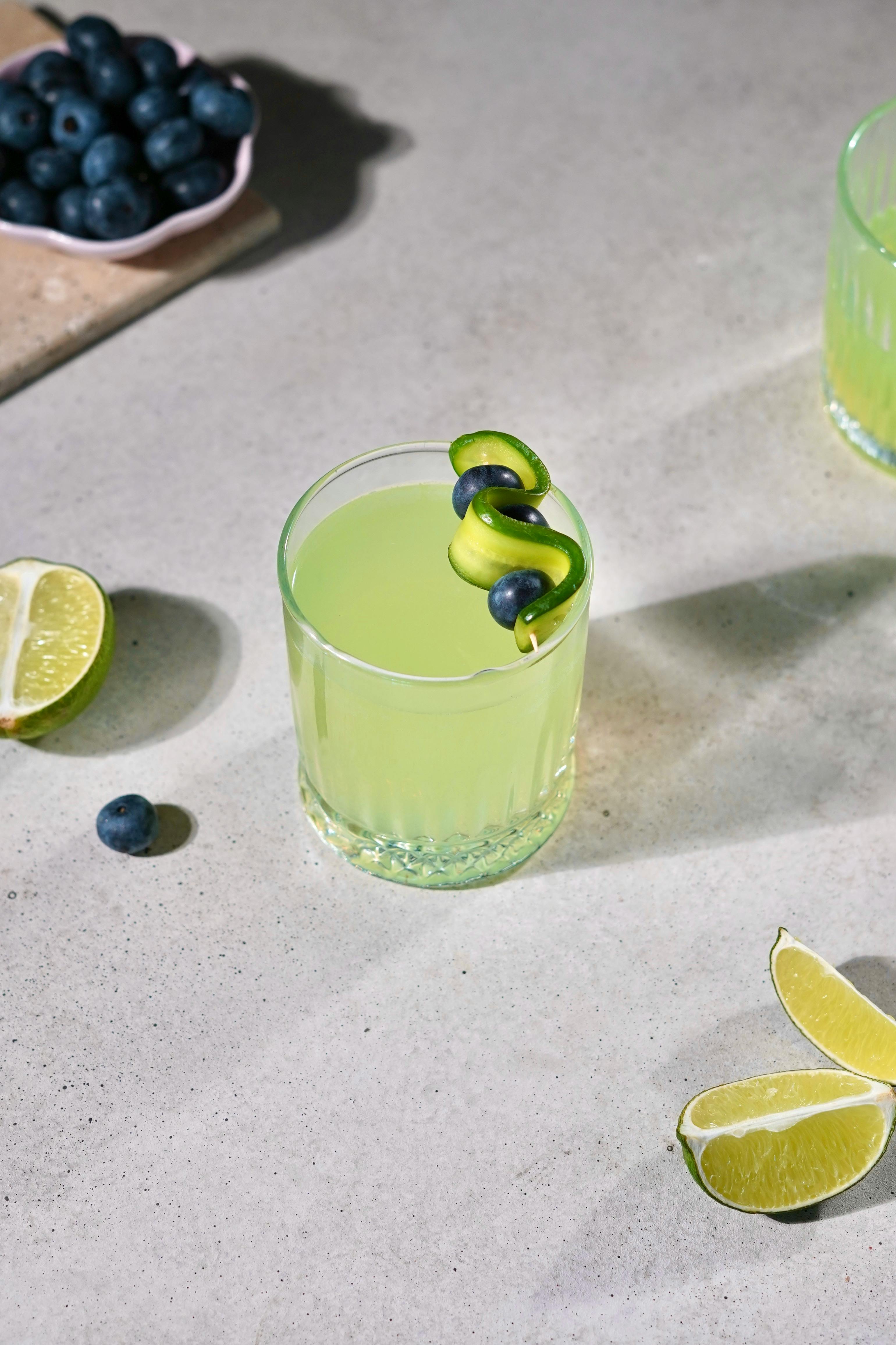 Chilled lime green cocktail with blueberry and lime garnish on concrete tabletop.