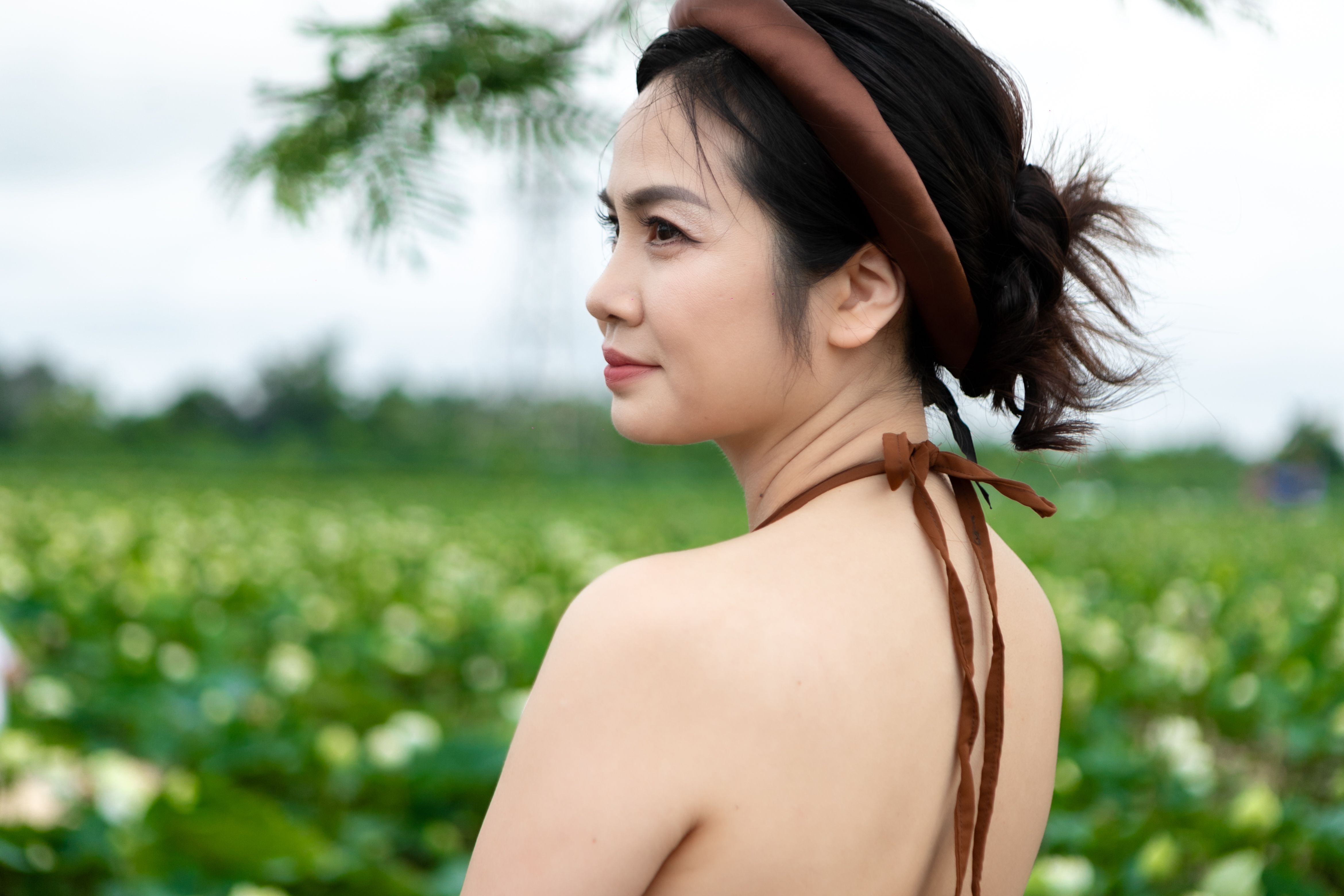 A woman with a brown headband posing outdoors in a serene field during summer.