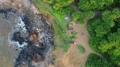 Free A stunning aerial view of a rocky shoreline and vibrant green landscape with visible people and bikes. Stock Photo