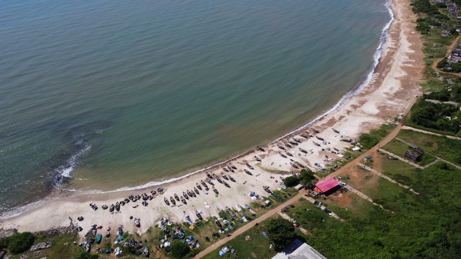 Aerial view capturing a serene coastal beach with fishing boats and lush greenery.