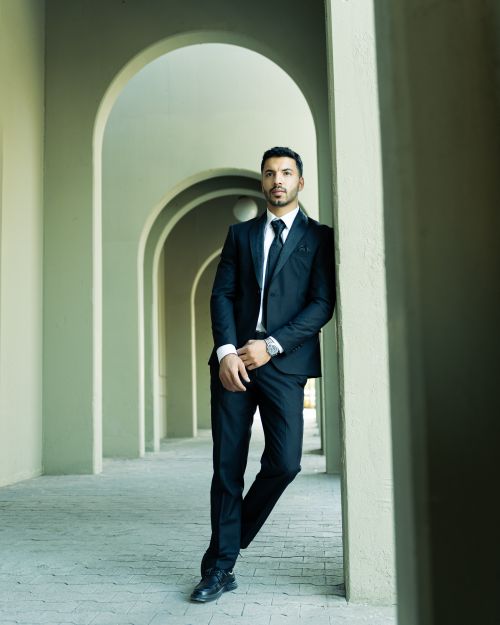 Free Stylish man in a black suit poses confidently beneath elegantly arched architecture. Stock Photo