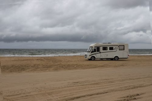 Free Camper parked on a tranquil beach in Dänemark under cloudy skies. Stock Photo