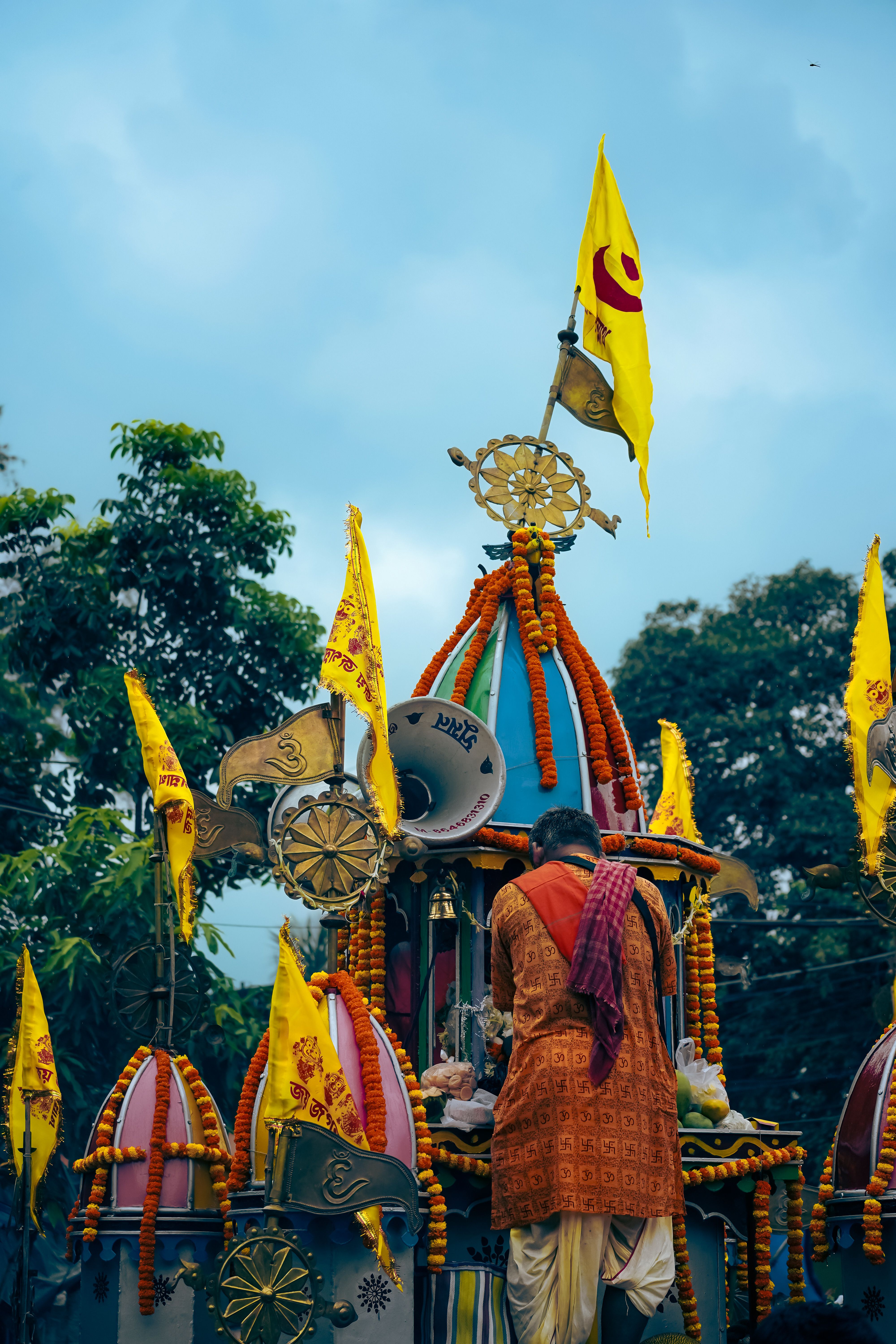 Vibrant Indian procession with decorated chariot and devotee under a cloudy sky.